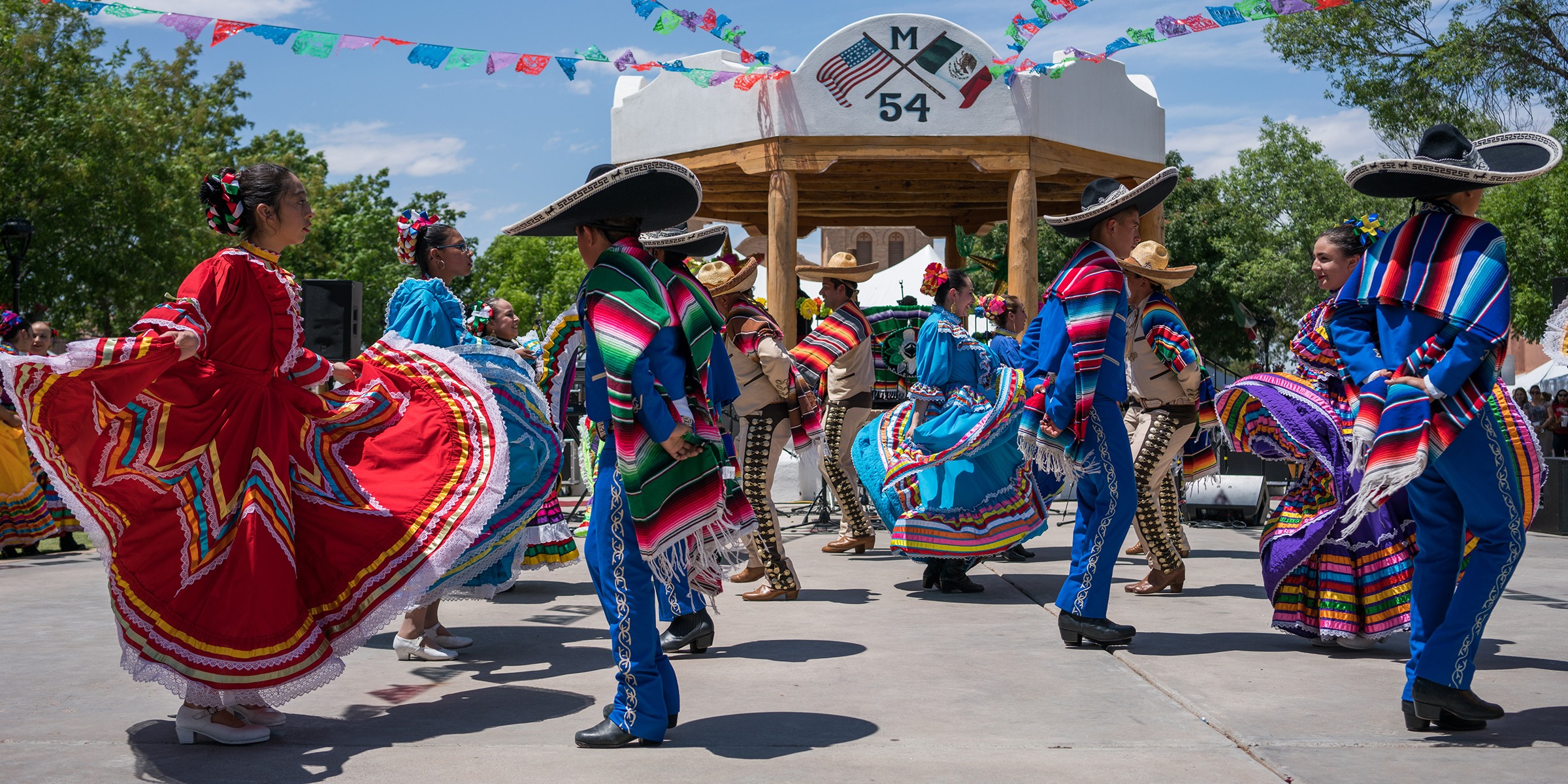 A parade celebrating Cinco de Mayo, with participants dressed in traditional Mexican attire, dancing and playing mariachi music.