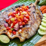 Ikan bakar sambal pedas yang disajikan dengan warna kecokelatan dan sambal merah di atasnya, siap disantap dengan nasi hangat